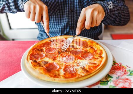 Fröhlicher hungriger Mann, der Pizza mit Gabel und Messer im italienischen Restaurant isst Stockfoto