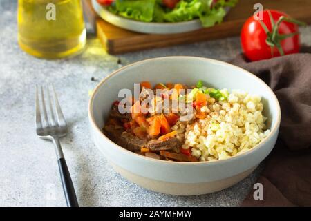 Gesundes Esskonzept. Rindfleisch mit Gemüse in Bulgur-Sauce und frischem Gemüsesalat auf einem hellen Steinteller. Stockfoto
