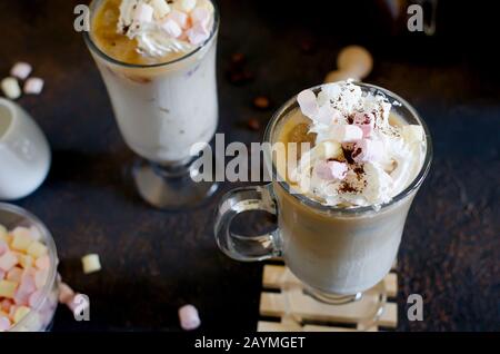 Sommerlicher Eiskaffee in hohen Gläsern mit Eiswürfeln, Milch oder Creamer und dekorierten Marshmallows, braunem Hintergrund und selektivem Fokus Stockfoto
