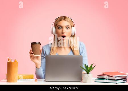 Schockierte blonde Mädchen, die mit einem Laptop auf die Kamera blickt Stockfoto