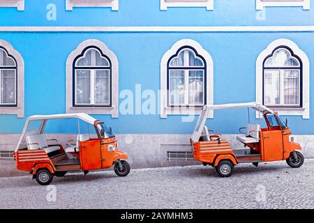 Tuk Tuk Vehikel vor blauem Fassadengebäude in Lissabon, Portugal. Tuktuk ist ein traditionelles Taxi auf Thailand und der beliebte Turistic Transport a Stockfoto