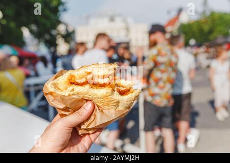 Großer Burger in der Hand am Hintergrund des Straßenfood-Festivals Stockfoto