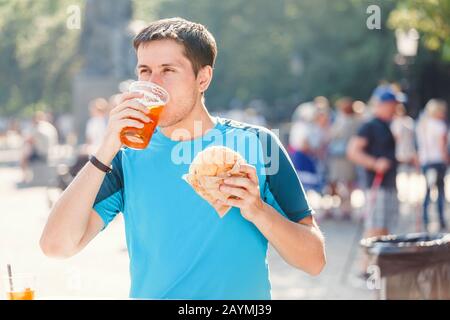 Mann im Freien, Der Burger Isst und Bier auf dem Straßenfest trinkt Stockfoto