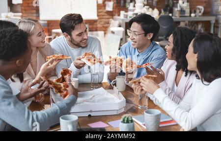 Freundliches internationales Team, das gemeinsam Pizza im Büro genießt Stockfoto