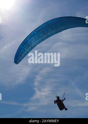 Ein Mann fliegt in seinem Gleitschirm vor blauem Himmel Stockfoto