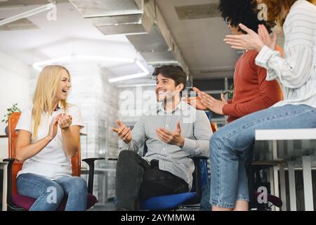 Positive Gruppe von Kollegen, die Briefing, Lachen und Klatschen haben Stockfoto