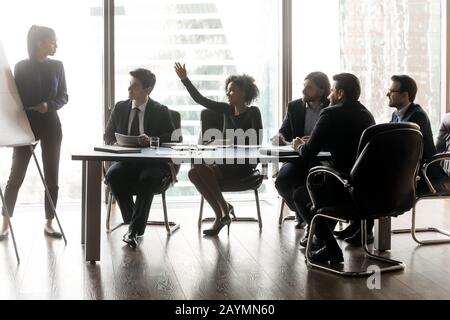 Lächelnde schwarze Geschäftsfrau, die die Hand hebt und die weibliche Hauptrolle im Sitzungssaal fragt. Stockfoto