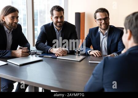 Bewerber sitzt vor drei glücklichen HR-Geschäftsleuten, die sprechen. Stockfoto