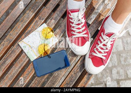 Reisezubehör Flachansicht auf einer Bank: Karte, Sonnenbrille ein Telefon mit roten Schuhen Stockfoto