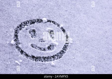 Lächelndes Emoticon auf dem ersten Schnee auf der Windschutzscheibe Stockfoto
