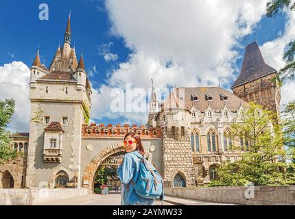 Fröhliche Touristin mit Rucksack auf Brücke vor dem Schloss Vajdahunyad in Budapest, Ungarn. Stockfoto