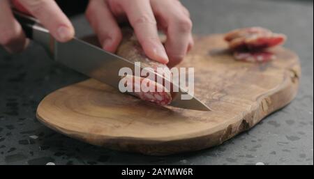 Man schlitzte Fuettenwurst auf olivem Holzbrett, breites Foto Stockfoto