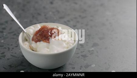 Hüttenkäse mit Feigenmarmalade und Joghurt in weißer Schüssel auf Betonoberfläche, breites Foto Stockfoto