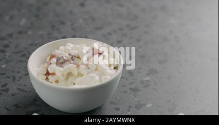 Hüttenkäse mit Feigenmarmalade und Joghurt in weißer Schüssel auf Betonoberfläche, breites Foto Stockfoto