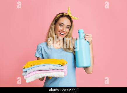 Das tausendjährige Mädchen hält gefaltete, saubere Sachen und Reinigungsmittel Stockfoto