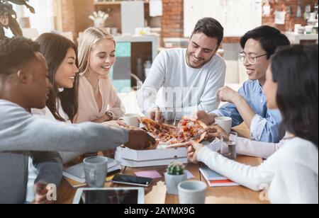 Fröhliche Kollegen essen im Büro zusammen Pizza Stockfoto