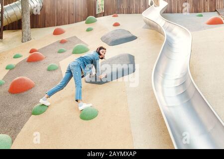 Eine infantile und glückliche Frau, die auf einer Kinderrutsche auf einem Spielplatz sitzt Stockfoto