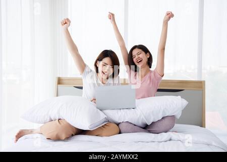 Zwei aufgeregte Asiaten sehen sich Laptop an und feiern ihren Sieg im Schlafzimmer. Konzept für Aktivitäten im Teenageralter oder im Freundeskreis, Lifestyle zu Hause. Stockfoto