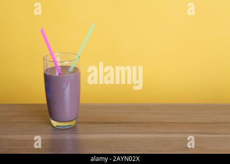 Ein halbes Pint Glas Schokoladenmilch mit zwei Strohhalmen auf Holztisch mit Copyspace auf gelbem Hintergrund Stockfoto