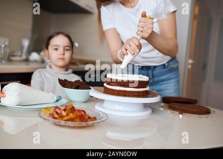 WWoman Hands quetscht Creme auf Kuchen, Schritt für Schritt Rezept für leckere Kuchen. Nahaufnahme zugeschnittenes Foto, nachdenkliches kleines Mädchen, das im Hintergrund des p sitzt Stockfoto