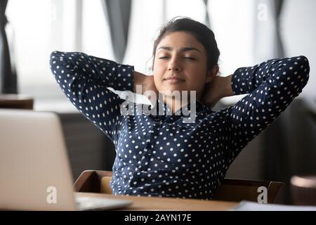 Müde ethnische Frauen entspannen sich am Arbeitsplatz im Stuhl Stockfoto