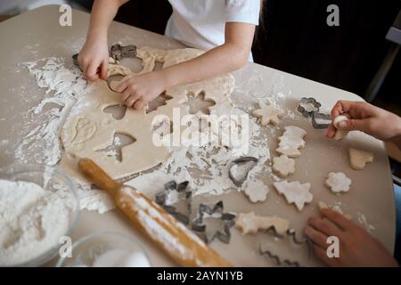 Kleines Kind trennt, schneidet nutzlosen Teig ab, nimmt Formen, Figuren aus Teig. Backprozess Plätzchen. Nahaufnahme des zugeschnittenen Fotos Stockfoto