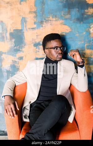 Profil Seitenansicht Portrait von fröhlichem Optimismus positiv gutaussehender afroamerikanischer Mann im Anzug isoliert über hellem Hintergrund in Orange sitzend Stockfoto