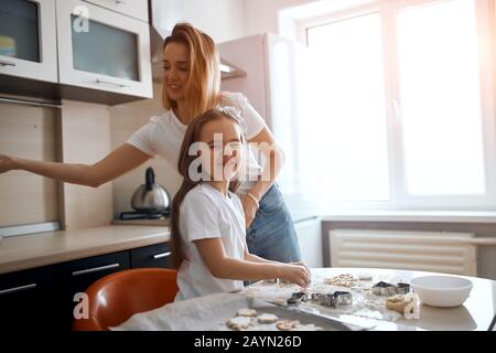 Lustige Mädchen mit Mehl an der Nase, die Gesichter macht, während sie mit Mama in der Küche arbeitet. Schließen Sie Foto.Copy-Platz Stockfoto