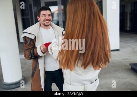 Junger glücklicher schwarzhaariger Mann mit bärtigen und Schnurrbart flirtet im Freien mit Ingwermädchen, Nahaufnahme. Werden Sie mich heiraten Nahaufnahme Foto Stockfoto