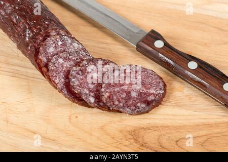 Trockenes Salami-Wurststäbchen und Messer auf Holzbrett mit Scheiben. Nahaufnahme. Draufsicht Stockfoto