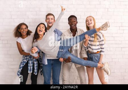 Fröhliche internationale Gruppe von Freunden, die asiatische Mädchen hochheben Stockfoto