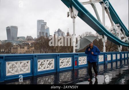 Ein Mann überquert die Tower Bridge in London bei einem schweren Regenfall, als Storm Dennis das Vereinigte Königreich trifft. Stockfoto