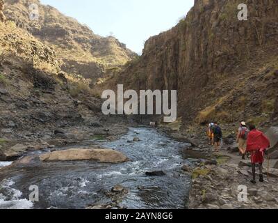 NGARE-SERO. Tansania - 20. AUGUST 2019: Der Touristen amd Maasai geht am Fluss Ngare Sero in der Nähe des Natron-Sees in Tansania, Afrika Stockfoto