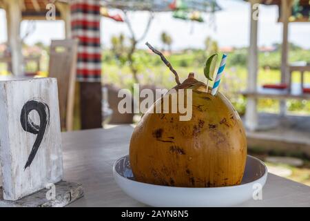 Frische Kokosnuss mit Papierstroh und Kalk in einem Café im Freien. Holztisch Nummer NEUN. Bali, Indonesien. Stockfoto