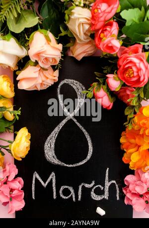 Die Aufschrift März 8 auf einem schwarzen Kelch, mehrfarbig Blumen rosa Hintergrund. Frauentag. Urlaub. Draufsicht Stockfoto