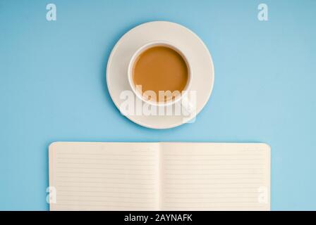 Weißes, offenes Notizbuch für Notizen, eine weiße Tasse Kaffee mit Milch auf blauem Hintergrund, Platz für Text Stockfoto