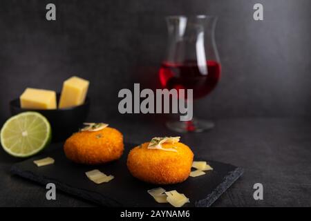 Hausgemachte Kroketten, gefüllt mit Käse mit Zitrone und einem Glas Rotwein. Stockfoto