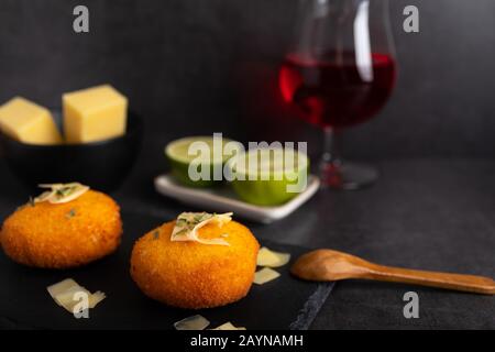 Hausgemachte Kroketten, gefüllt mit Käse mit Zitrone und einem Glas Rotwein. Stockfoto