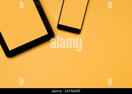 Schwarzes Tablet und schwarzes Telefon auf orangefarbenem Hintergrund. Platz für Text. Draufsicht. Flaches Lay Stockfoto