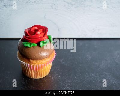 Einzelner Vanilleschrank mit Schokoladenaufschäumen, mit roter Rose und grünen Blättern vor schwarzem Schiefer und grauem Shiplap-Hintergrund, perfektes f Stockfoto