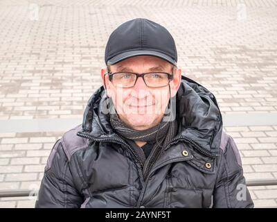 Ein Mann mit Brille und einer Kappe auf einer Bank. Menschen. Winterkleidung. Platz für Text. Stadtleben Stockfoto