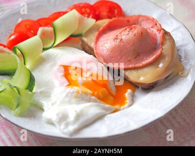 Fertigfrühstück aus Eiern mit flüssigem Eigelb, Wurst- und Käsesandwich mit Tomaten und Gurkenscheiben Stockfoto