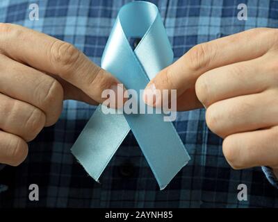 Ein Mann in einem Plaid Hemd hält zwei Hände blaues Band Symbol des Prostatakrebsbewusstseins.Konzept der Medizin und bemannt Gesundheitspflege Stockfoto