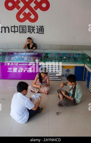 Kinder, die Kartenspiel in einem Handyladen in einem neuen Teil der Stadt Fengdu spielen, das für Menschen gebaut wurde, die aufgrund des c umgesiedelt werden mussten Stockfoto