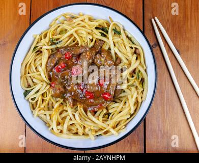 Spicy Chili Rind mit gebratenen Nudeln in eine Schüssel mit Stäbchen auf einen hölzernen Tisch aus einem Overhead Perspektive Stockfoto