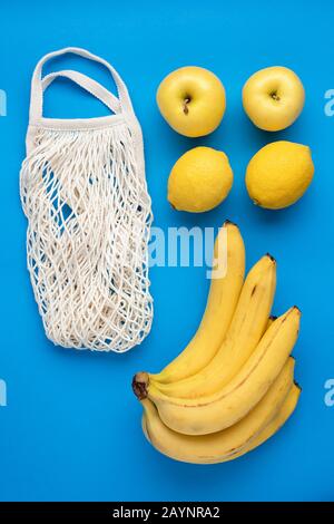 Gelbe Bio-Früchte Banane, apfel, Zitrone und Null Abfall wiederverwendbare Mesh-Einkaufstasche auf blauem Hintergrund. Kreatives Flachlay-Konzept von Null Abfall, eco Stockfoto