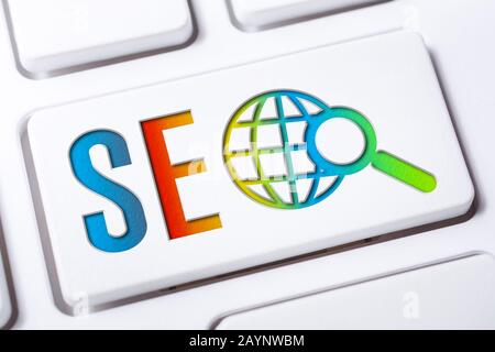 Bunt SEO Search Engine Optimization Button Mit Globe Und Lupe Auf EINER weißen Tastatur, Business Marketing Konzept Stockfoto
