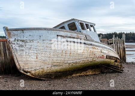 Ein verunglücktes Boot am Ufer neben einem verfallenen Kai. Sowohl Boot als auch Wharf sind in sehr schlechter Form und fallen auseinander. Nahansicht. Ebbe. Stockfoto