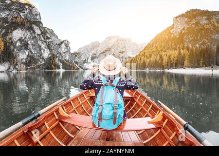 Fröhliche asiatin, die in einem Vintage-Boot aus Holz sitzt, schwimmt und segelt auf einem Braies See in den italienischen Alpen, Reise- und Traumferienkonzept Stockfoto