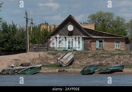 Holzhaus am Ufer des Flusses mit Booten und Satellitenschüssel auf dem Dach, Region Astrachan, Russland Stockfoto